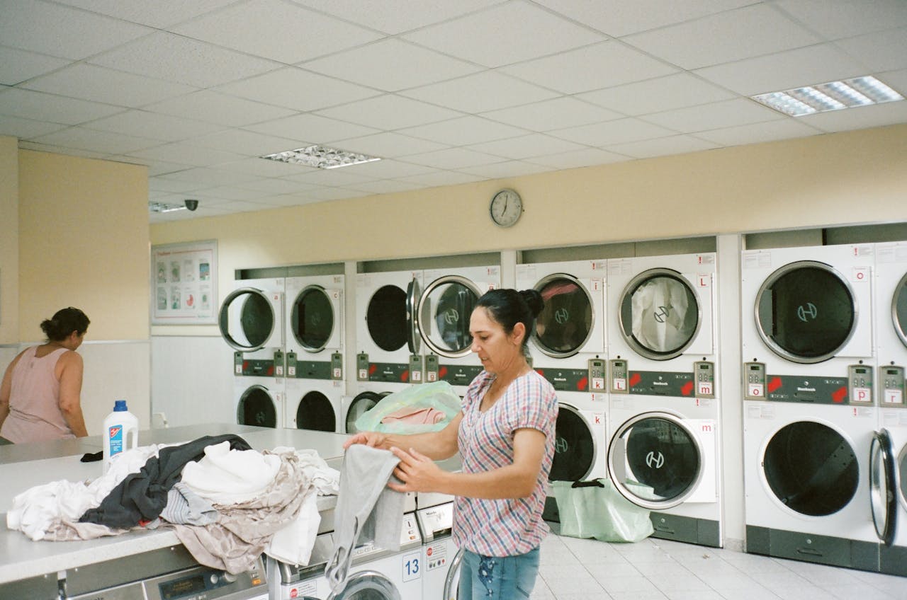 services-01 A woman folding clothes in a modern laundromat with various washing machines in the background.