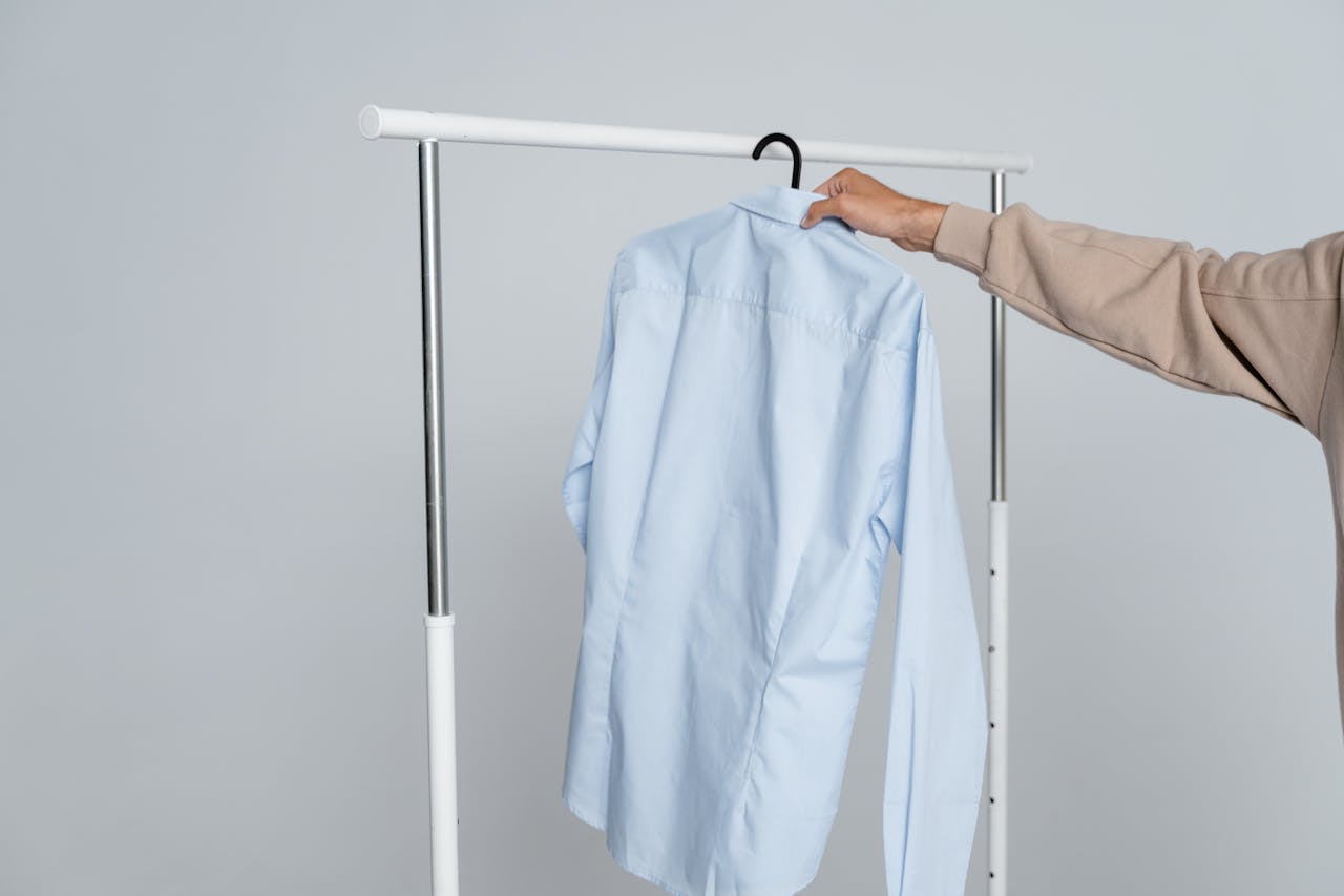 services-01 A person holding a blue shirt on a rack against a neutral background.